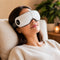 Person using an ergonomic, foldable eye massager with thermal pads and Bluetooth connectivity for relaxation.